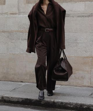 Annemiek Kessels wearing a brown shirt, pants, belt, sweater, The Row Margaux bag, and loafers.