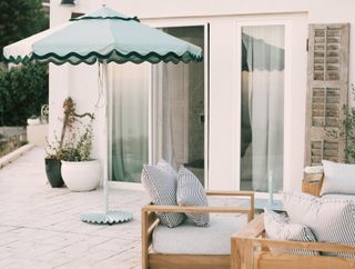 A sun umbrella in green with patio furniture placed outdoors. Planters also sit outside the home.