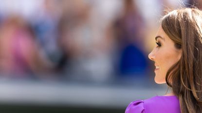 A shot of Kate Middleton from the back wearing a purple dress and looking to the side smiling 