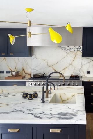 blue kitchen with marble countertops and backsplashs and a sink in the island