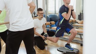 Trainer helping man perform lunge exercise on a wobble board