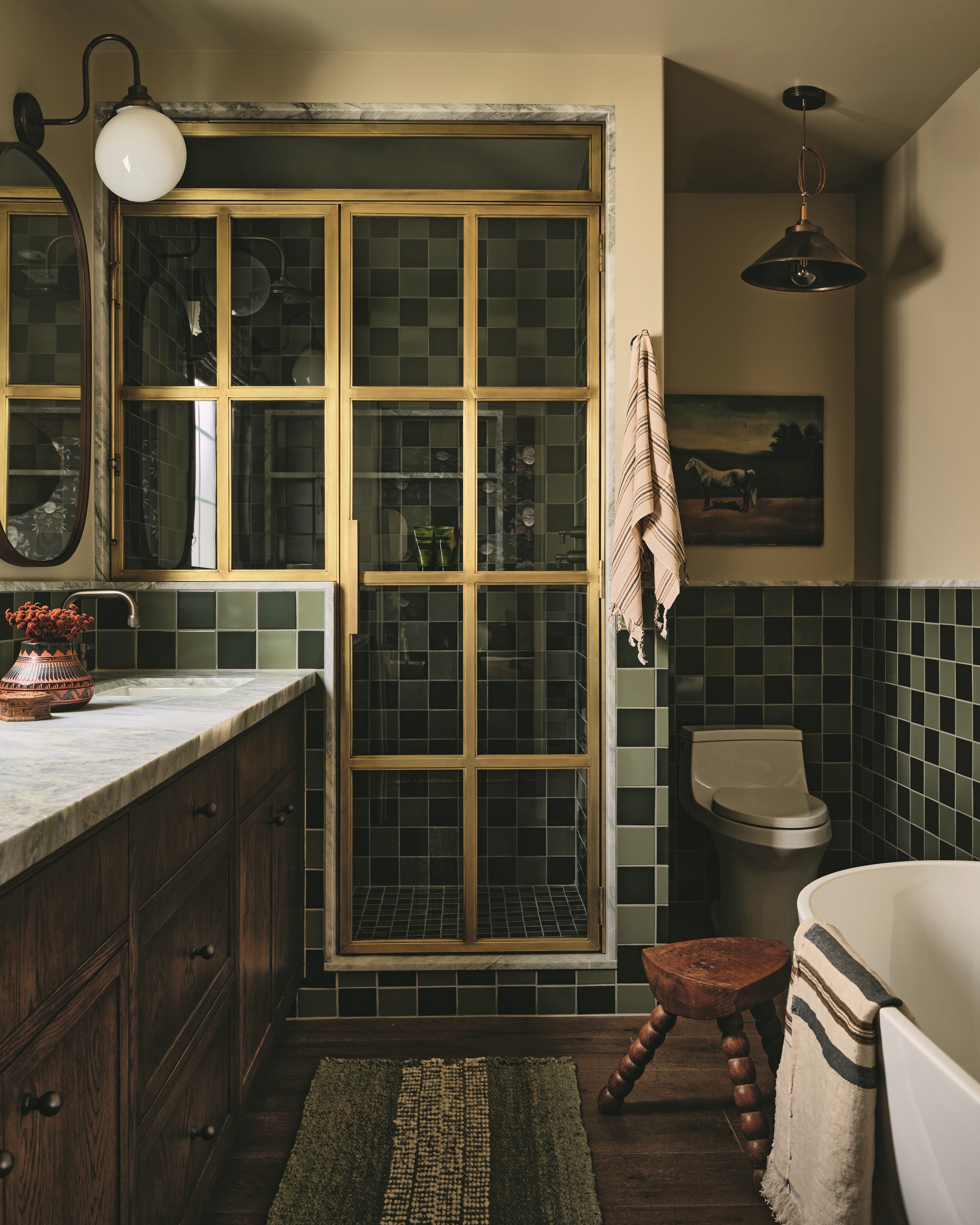modern bathroom with checkered tiles, enclosed shower with brass doors, a bathroom rug, bobbin stool, freestanding bath, and marble and timber vanity