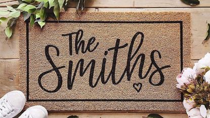 Customat Personalised Door Mat on the floor 'The Smiths', one of the best indoor doormats on our list, with flowers and shoes surrounding it