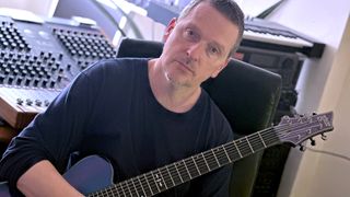 Justin Broadrick poses in his home studio with a Schecter eight-string electric guitar