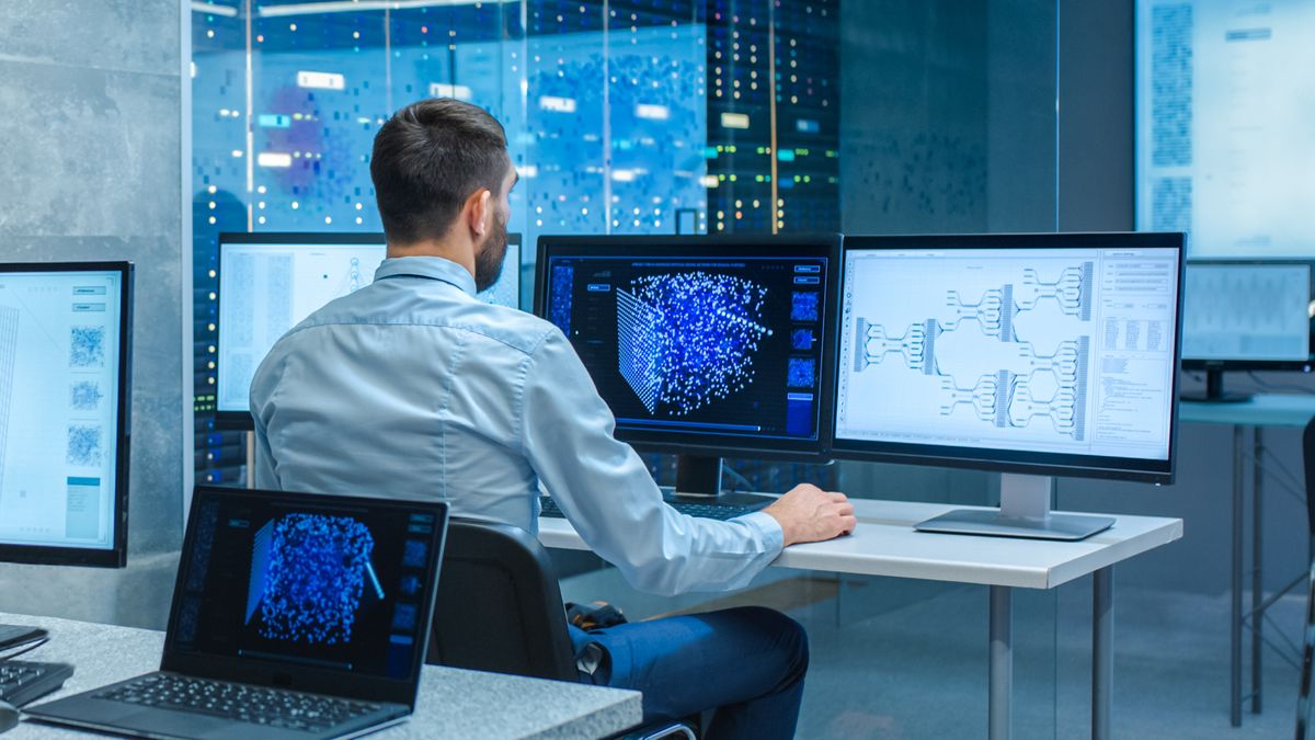 Computer engineer sat at desk with three monitors