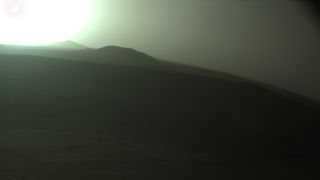 a sunset seen through a hazy, light-brown sky above a distant ridgeline