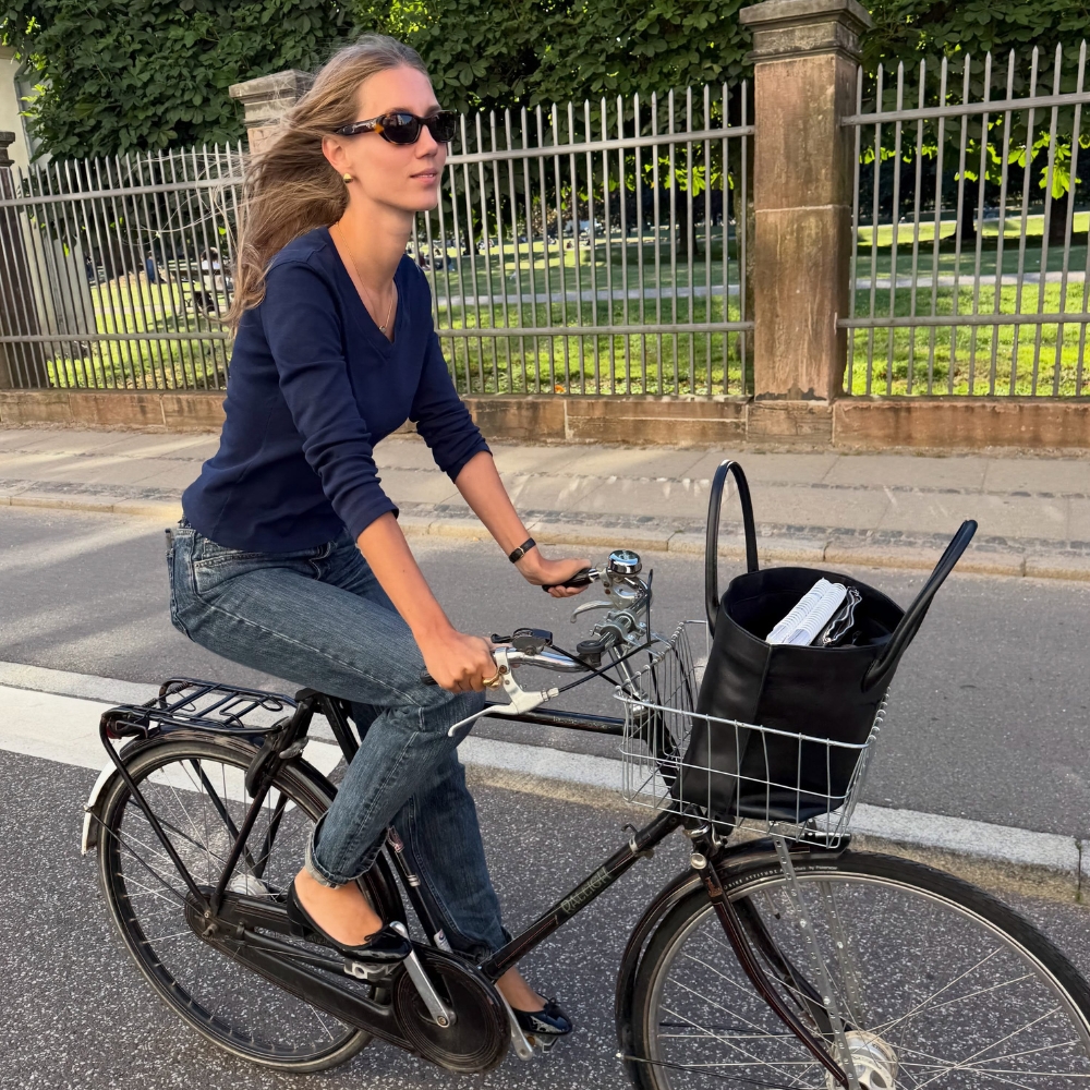 Influencer @amaliemoosgaard rides a bike wearing a v-neck knit with skinny jeans and black ballet flats.
