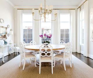 Circular wooden dining table, white cushioned dining chairs, white curtains