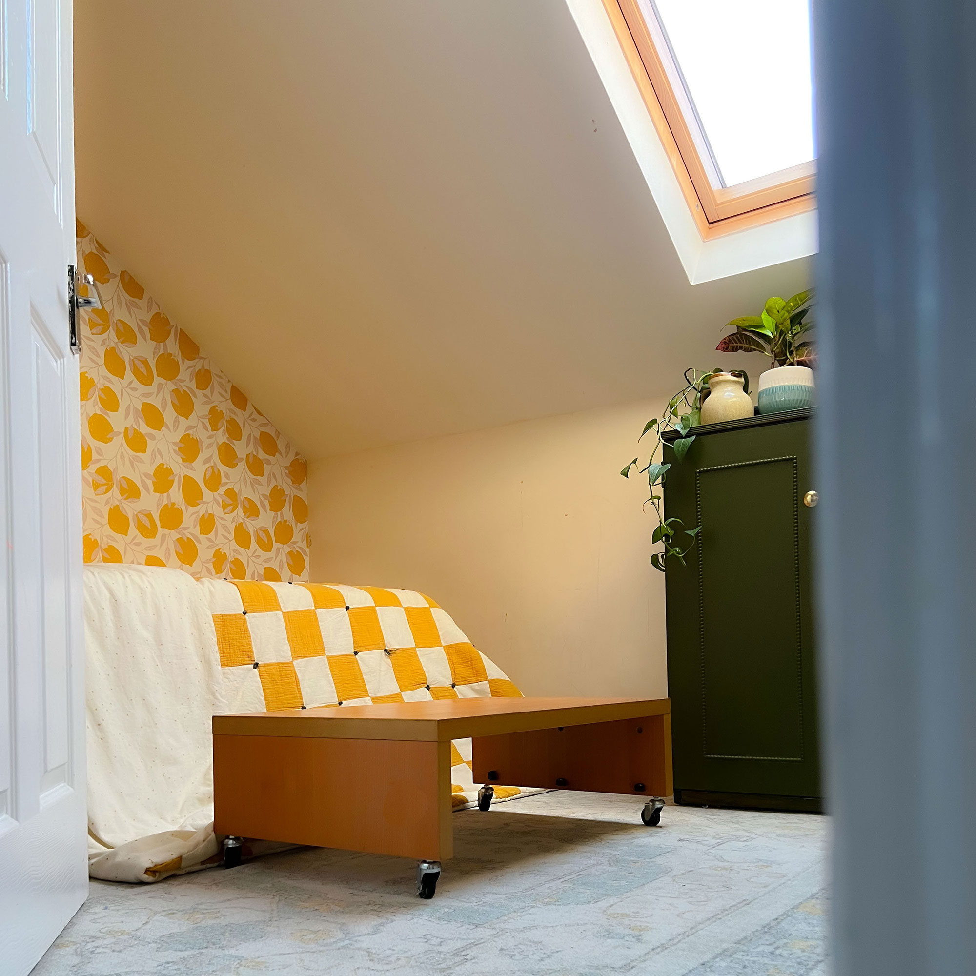 Wooden platform on castor wheels on rug beside bed in eaves room