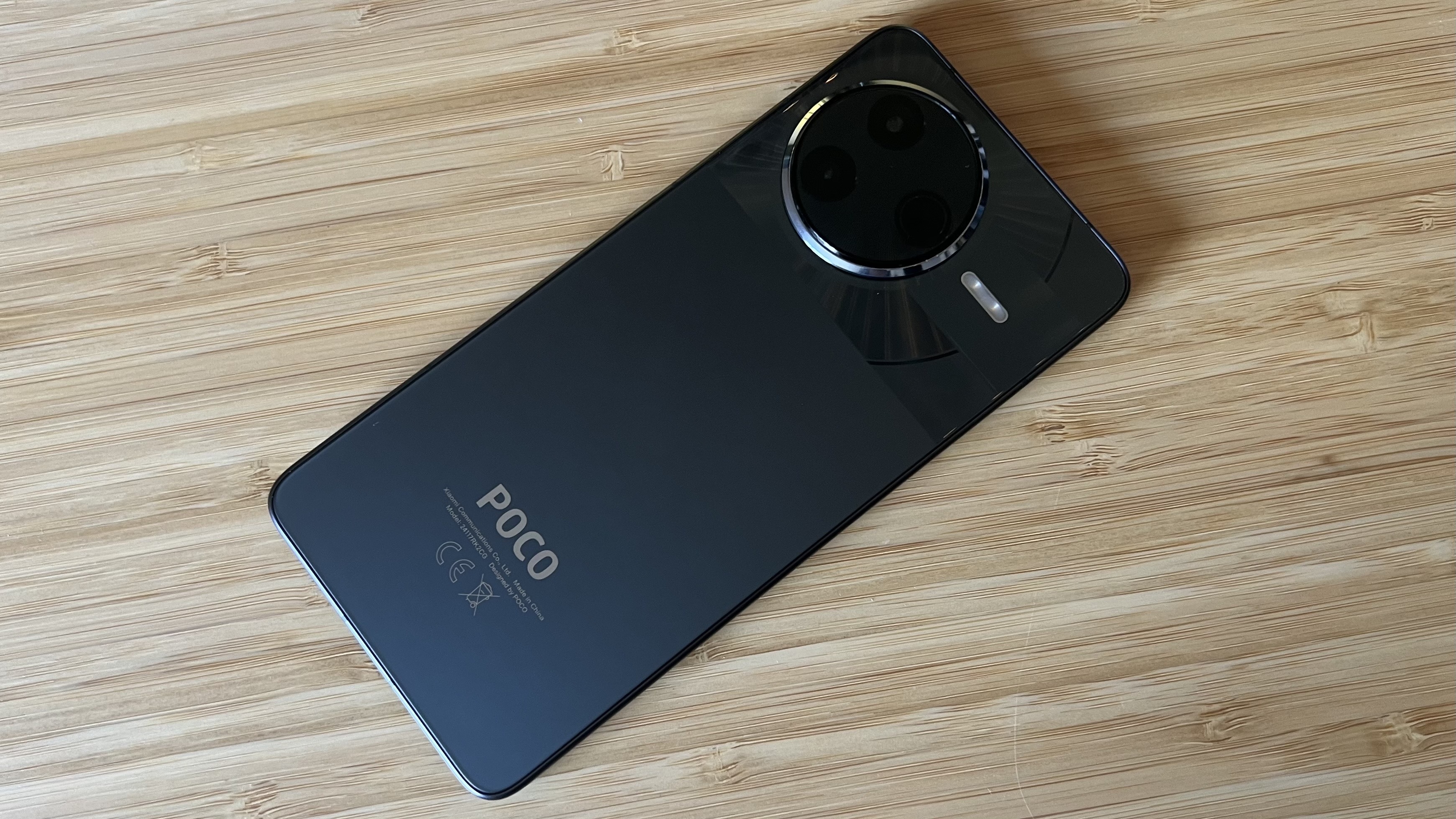 Poco F7 Pro on a wooden desk face-down, showing back panel and camera lens
