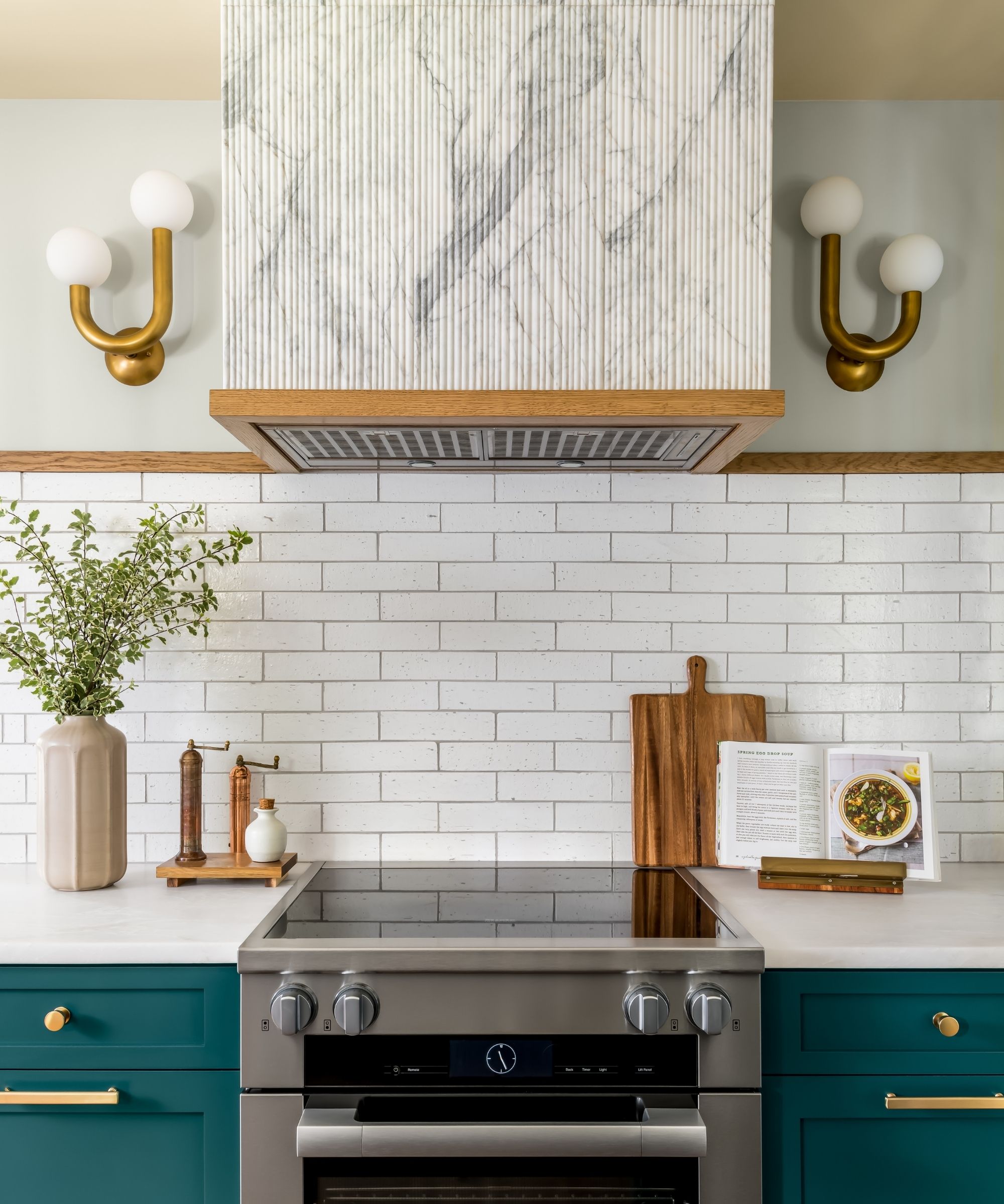 A green and white kitchen with sculptural wall lights by the cooktop