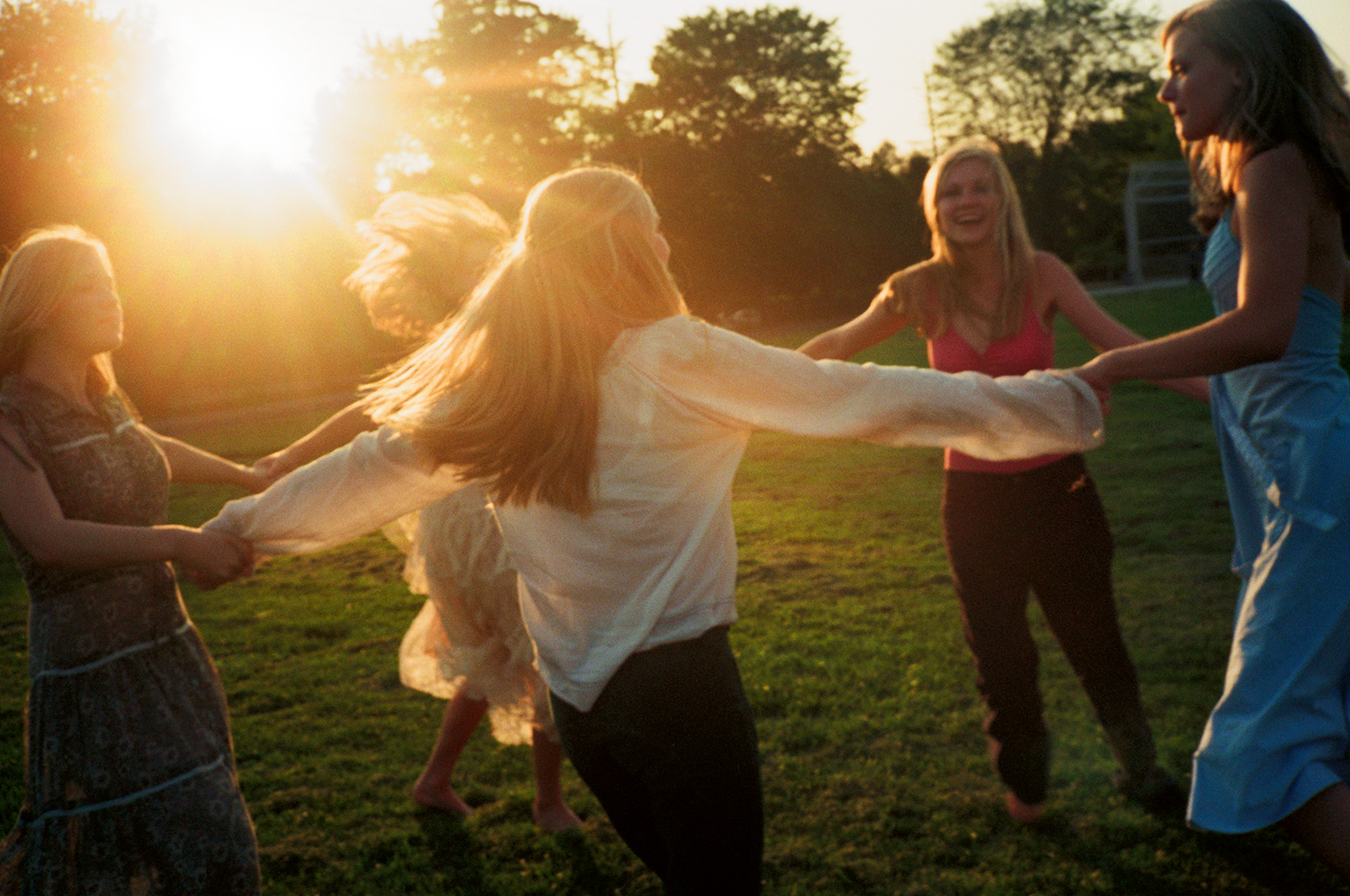 women, arms linked, dancing in a circle at sunset