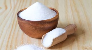 Sugar in a wooden bowl and in a measuring spoon
