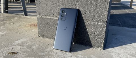 A OnePlus 9 from the back, leaning against a brick pillar
