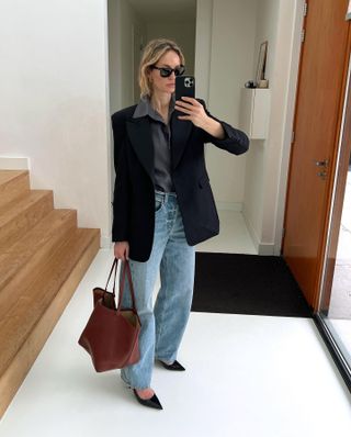 Woman in hall wears blazer, shirt, jeans and slingback heels