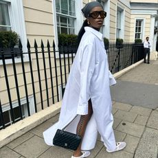 Woman wears a long white shirt dress, Alaia open weave Mary Janes, Chanel purse and hair scarf.