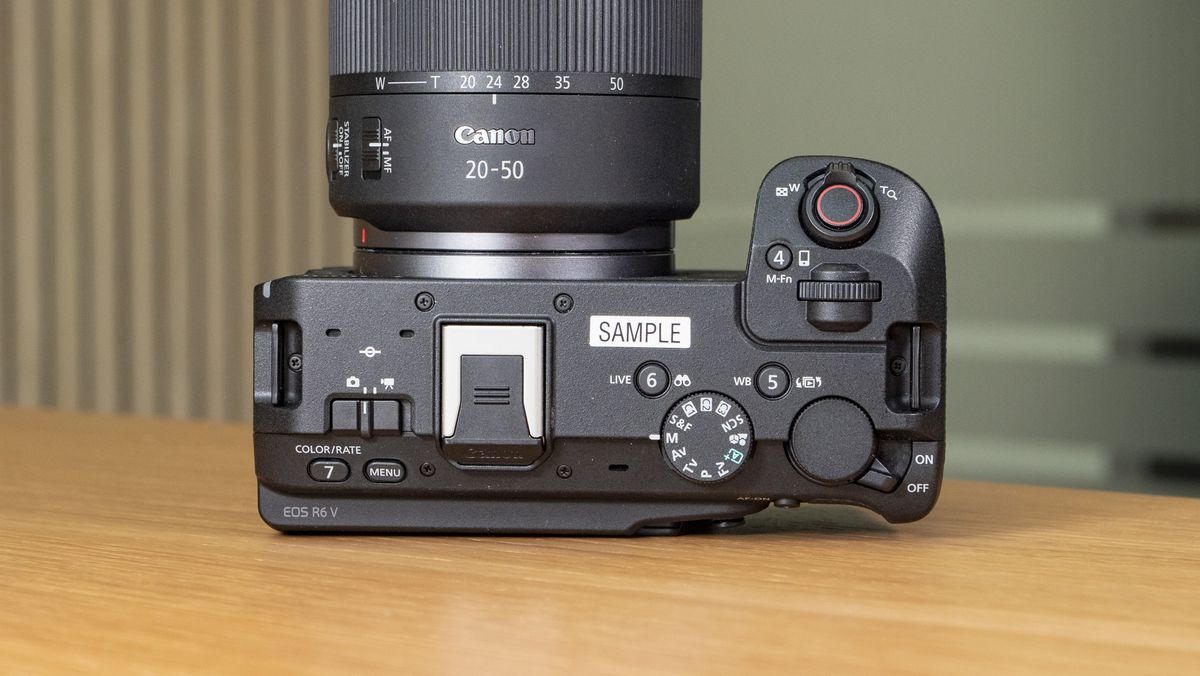 The Canon EOS R6 V mirrorless camera on a wooden table with a pine-slatted backdrop, view of the top plate