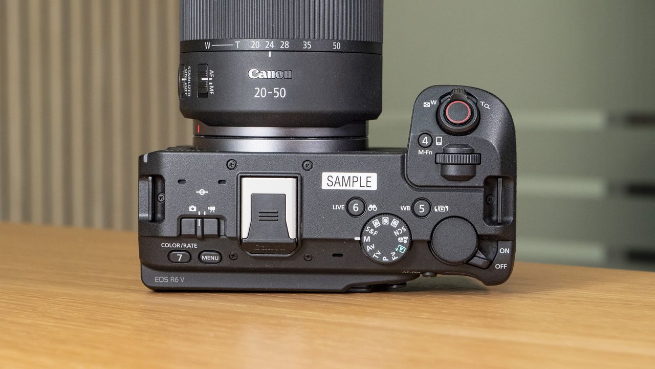 The Canon EOS R6 V mirrorless camera on a wooden table with a pine-slatted backdrop, view of the top plate