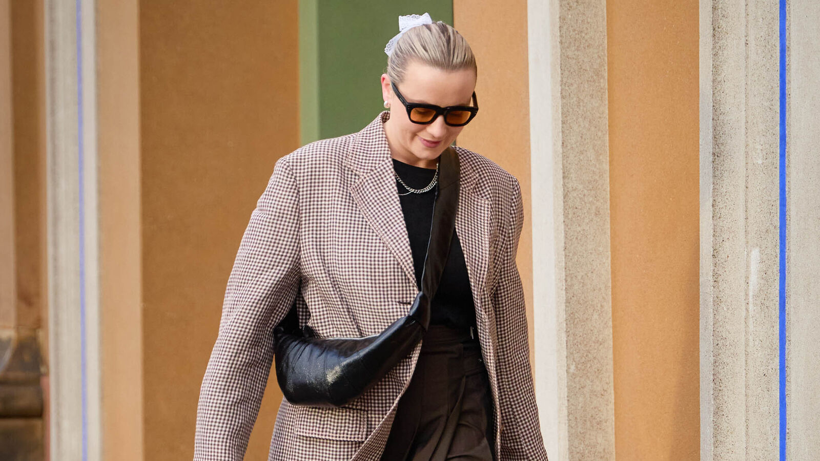 woman wears a maxi brown dress, a blazer, sneakers, and a cross-body handbag