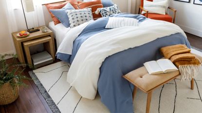 Alaca Area Rug from Boutique rugs in black and cream underneath bed dressed in blue and white bedding with red pillows and wooden end bench