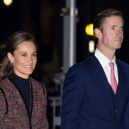 Pippa Middleton wears a black top with a mottled red jacket and her husband James Matthews wears a navy suit, white shirt, and red tie