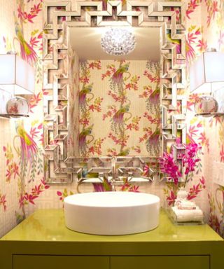 A green bathroom sink in front of pink tropical wallpaper and a mirror