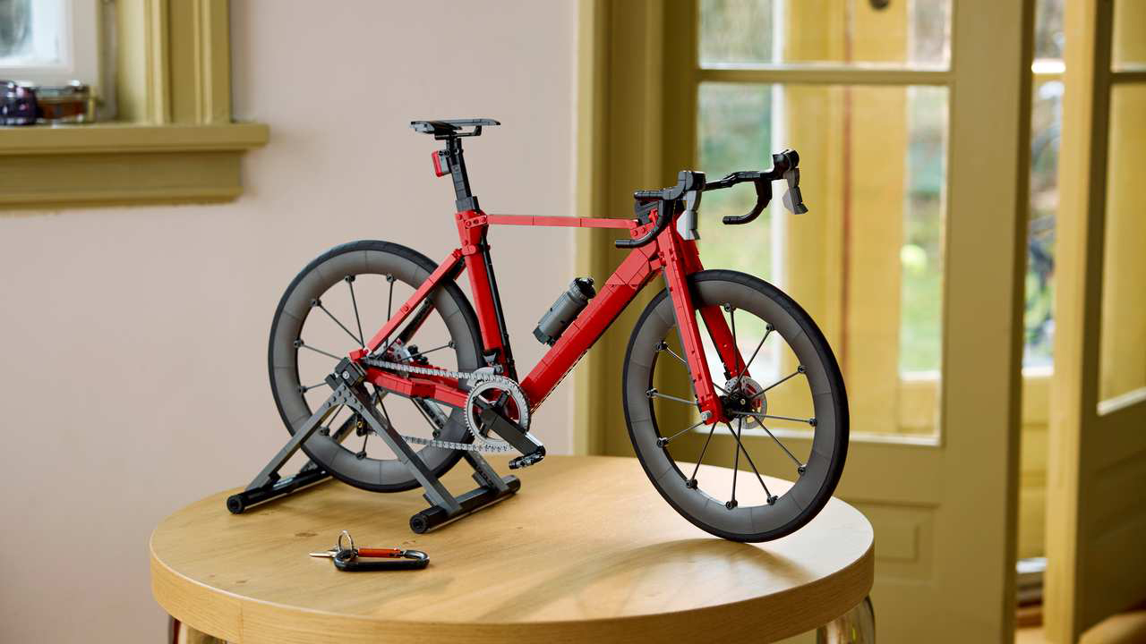 Lego Icons Road Bike, 11380. A lego road bike in red with black wheels and resting a lego smart trainers, having been completed and sitting on a table.