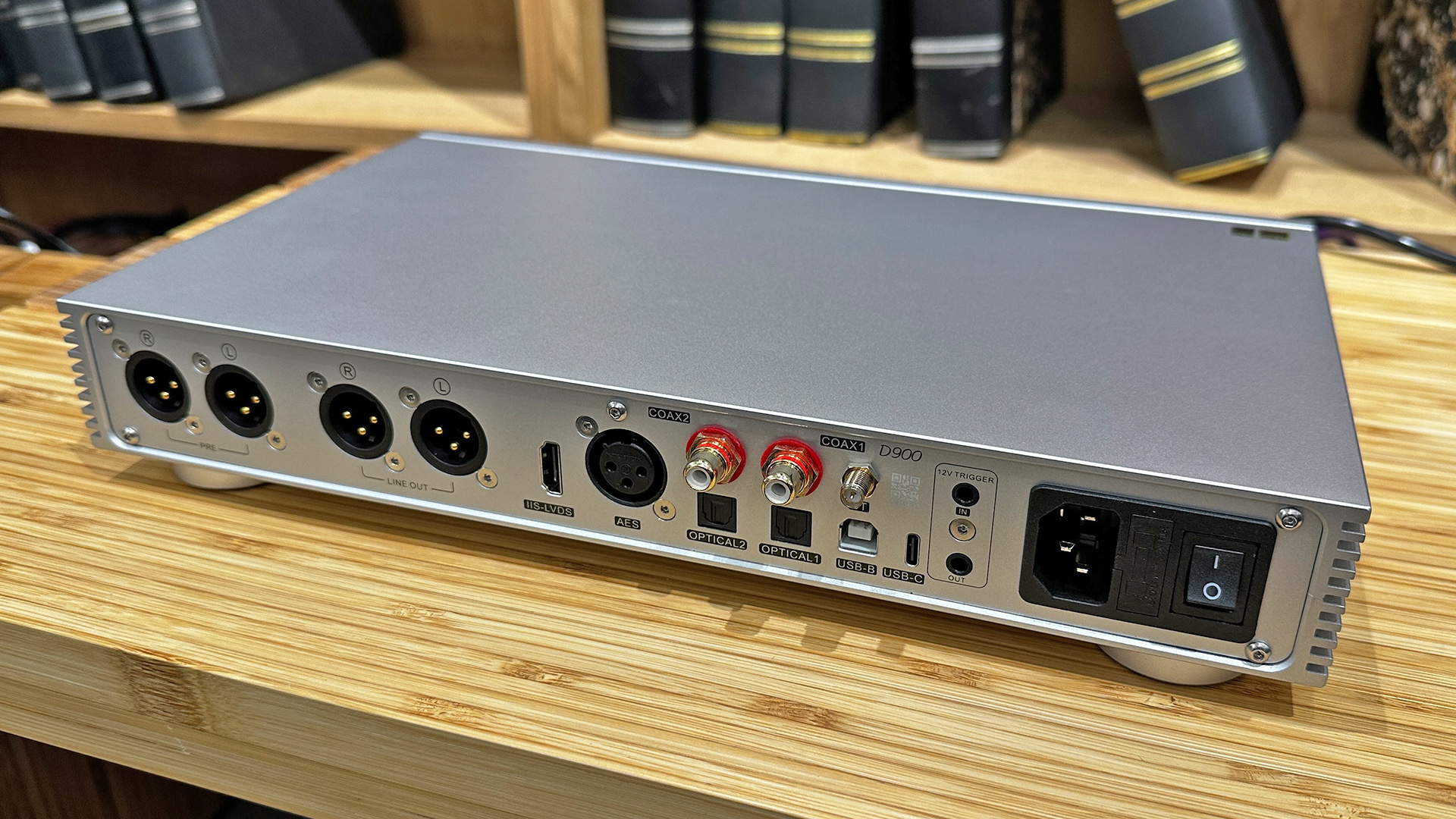 Topping Audio D900 DAC on wooden hi-fi rack in front of bookcase, rear of unit showing connections