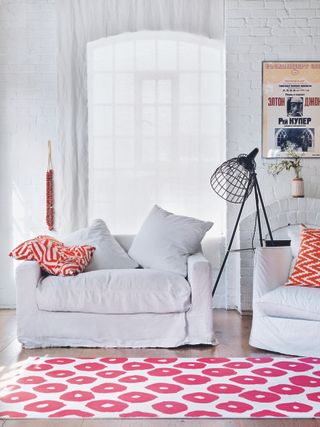 White living room with white rug with pink spots, and white comfy armchair with red patterned cushions