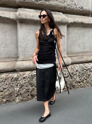 a photo of a woman wearing black and white layered tanks with black leather skirt and white shoulder bag and margiela tabi toe ballet flats