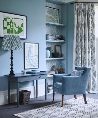 A blue living room with pastel blue walls, a matching desk, armchair and built-in alcove bookshelf.