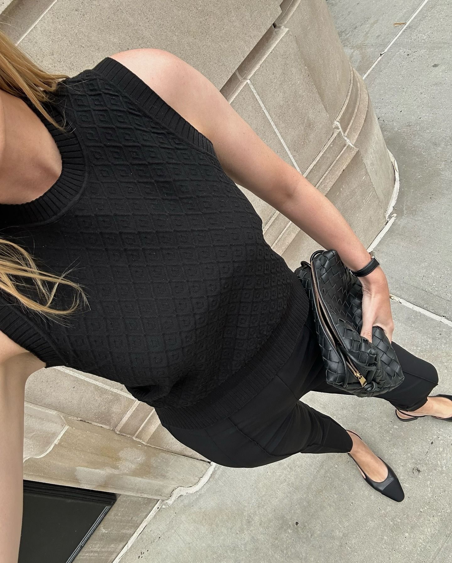 Woman wears black cigarette pants, black sweater shell, Chanel cap-toe slingbacks and Bottega Veneta clutch.