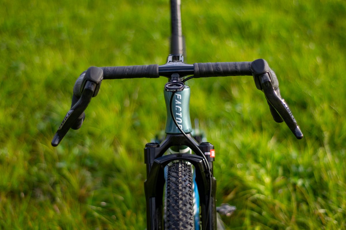 A blue Factor Sarana gravel bike in a grassy field with a hedge in the background