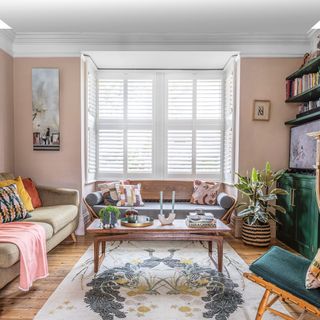 Pink living room with shutters at bay window, double sofas and wooden coffee table