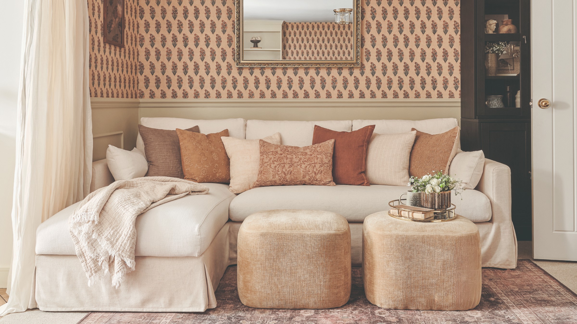 A living room with half panelled and half wallpaper-covered walls and a cream chaise sofa 