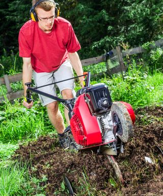 adult using a rotary tiller in a vegetable garden wearing goggles and ear defenders