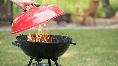 person holding the lid over a lit charcoal grill