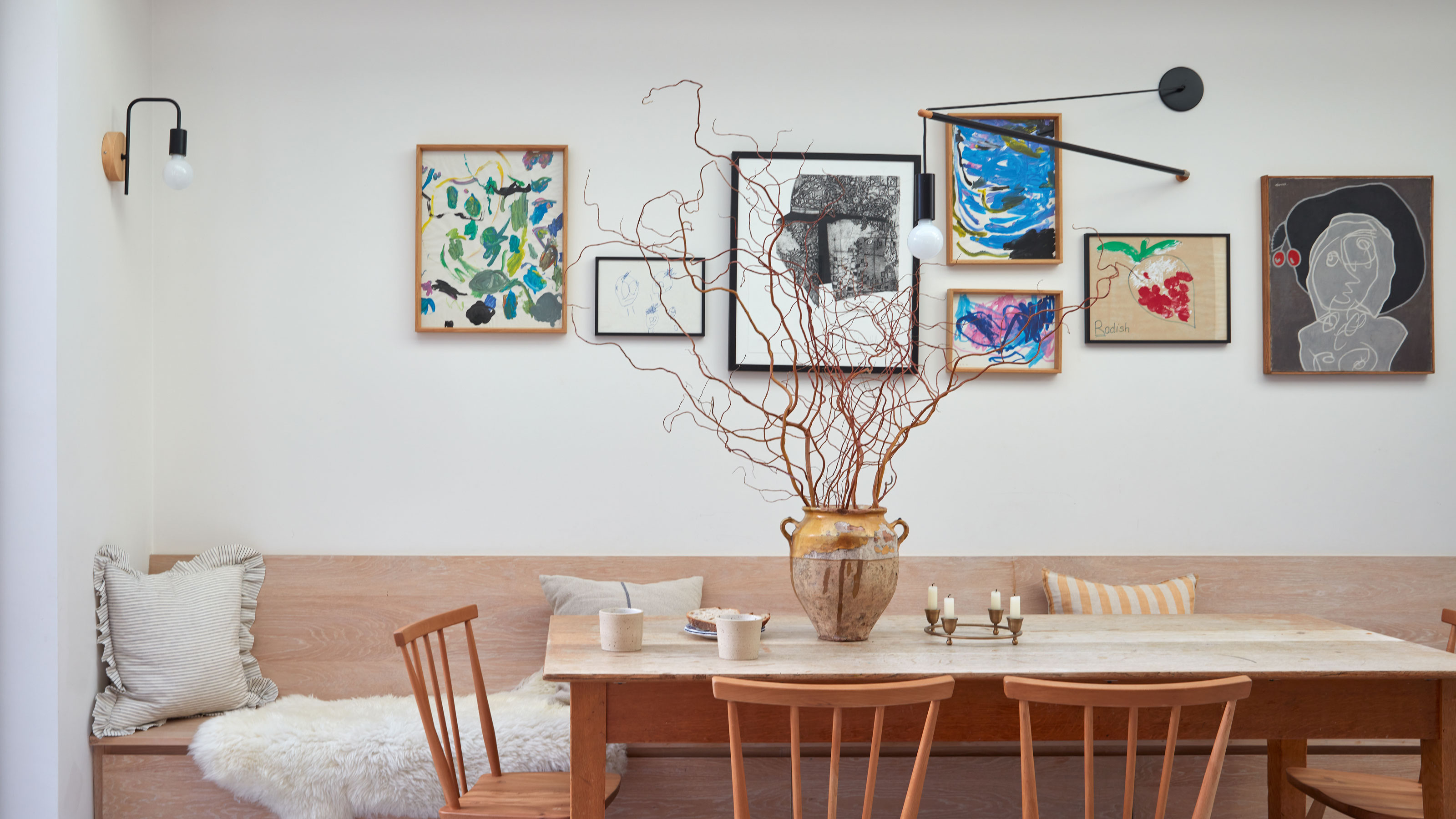 White dining area with wooden table and chairs, gallery wall, lamp and ceramic vase