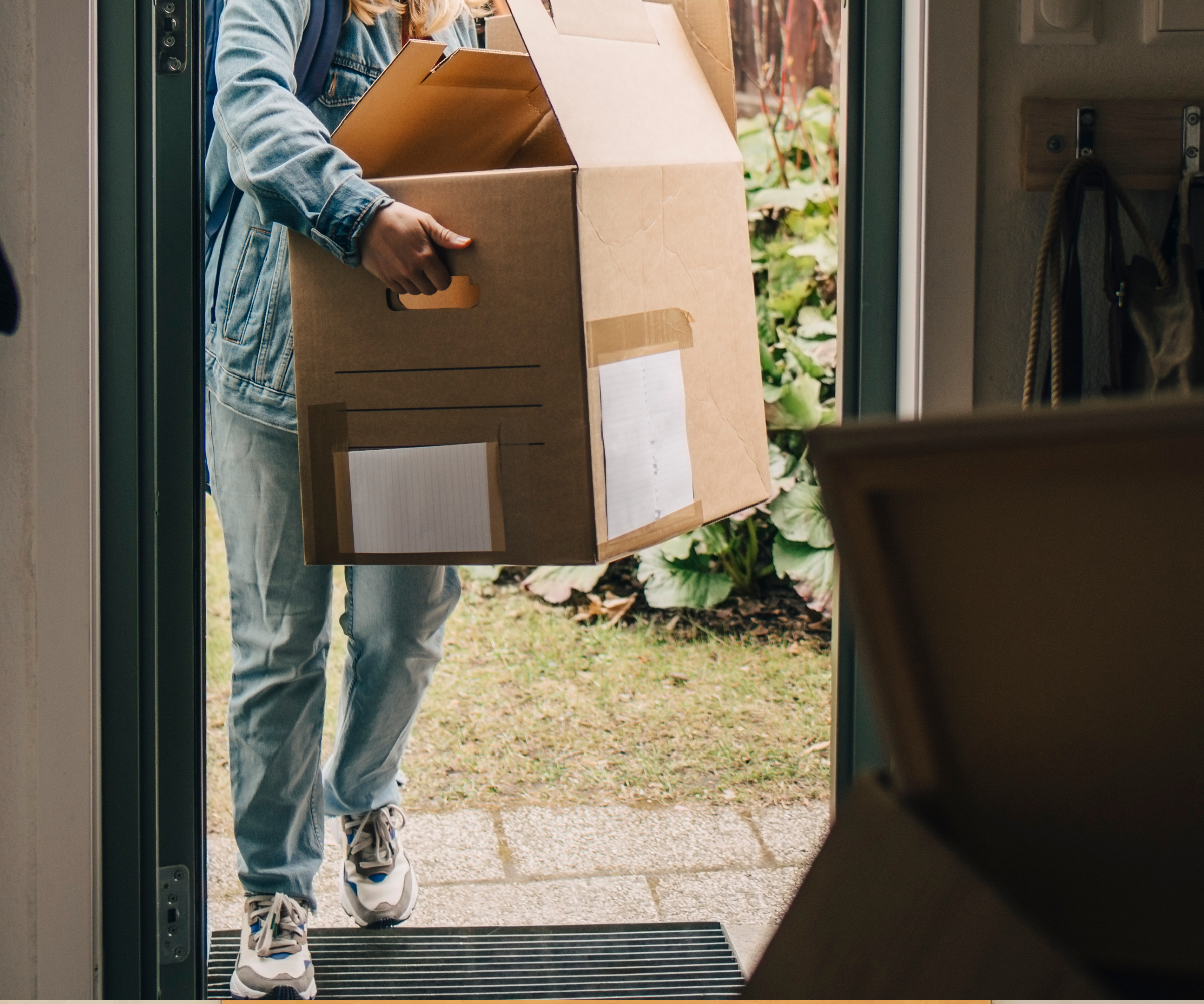Full length of young woman carrying box while walking in through doorway