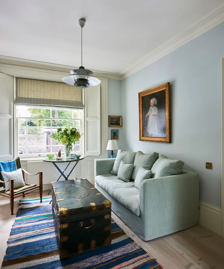 A green sofa next to a wooden trunk in a living room with a pendant light