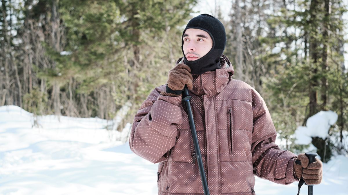 man wearing balaclava hiking or skiing in local forest on sunny winter day looking away