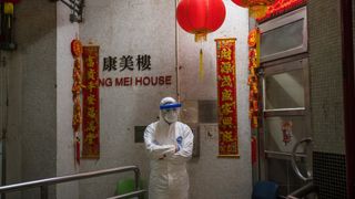 An official wearing protective gear stands guard outside an entrance to the Hong Mei House residential building at Cheung Hong Estate in Hong Kong on Feb. 11, 2020, following the evacuation of more than 100 people from the housing block after residents in two different apartments tested positive for the new coronavirus.