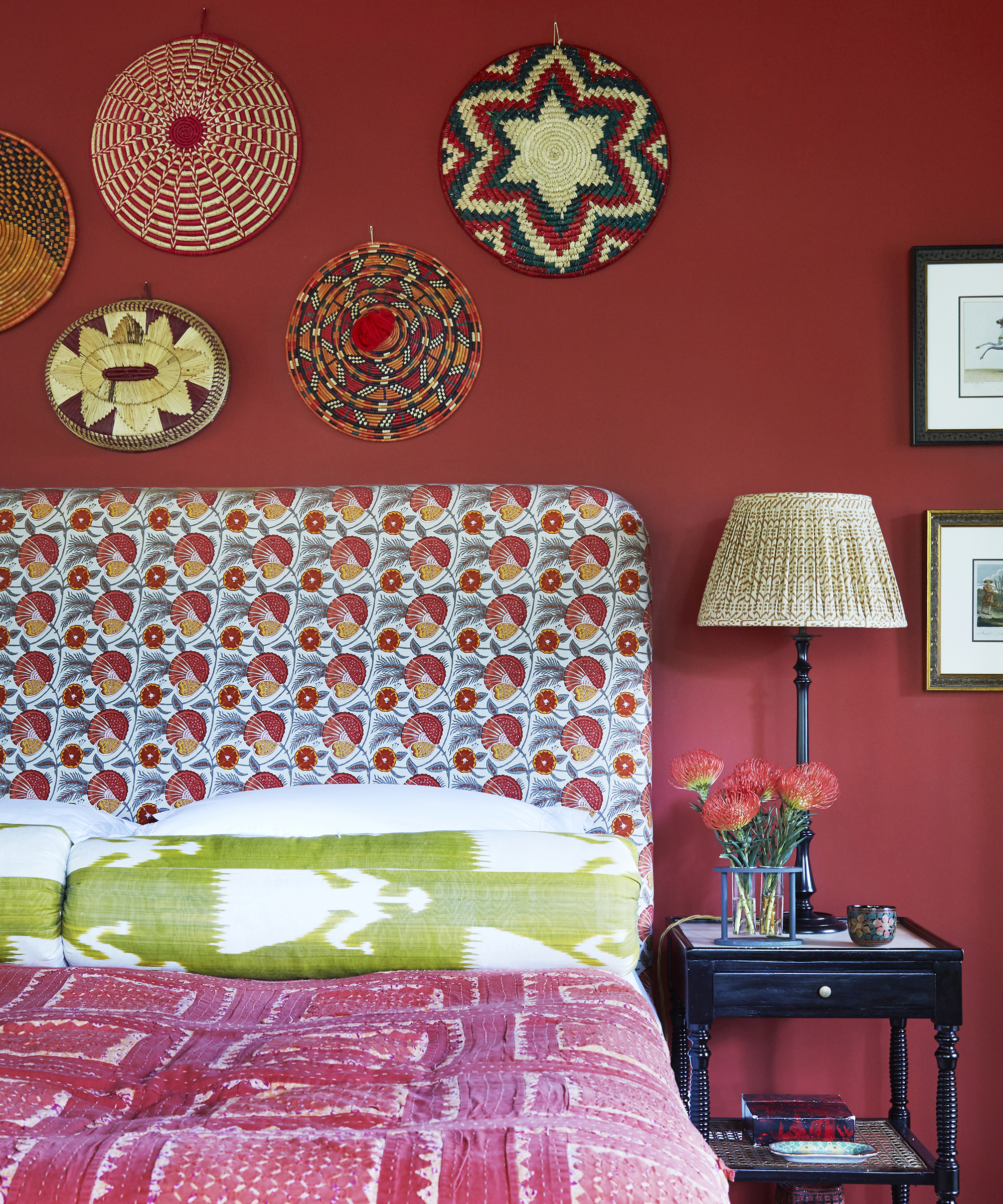 An example of bohemian bedroom ideas showing a bedroom with a red wall and a floral headboard with ikat prints and basketwork plates