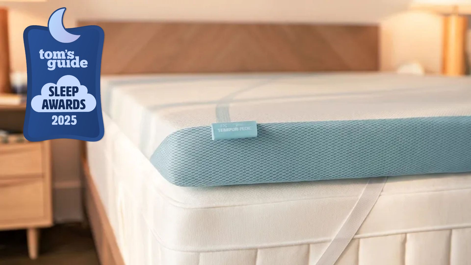 A close-up image of the bottom left-hand corner of the Tempur-Adapt + Cooling Mattress Topper attached to a white mattress. In the foreground, there is a Tom's Guide Sleep Awards 2025 badge with a crescent moon and a cloud illustration. 