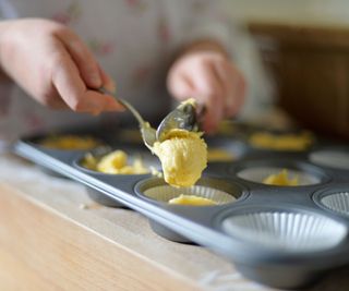 A woman scooping muffin batter into a baking tray.