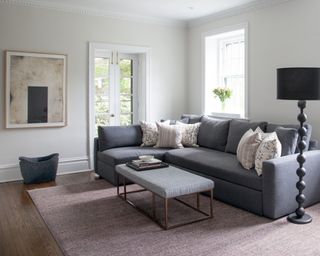 A living room with large grey corner sofa, pale pink rug, painting on the wall and tall statement lamp