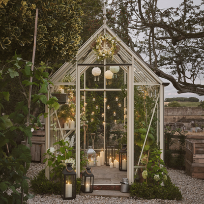 White greenhouse in garden decorating with lanterns and festoon lights.