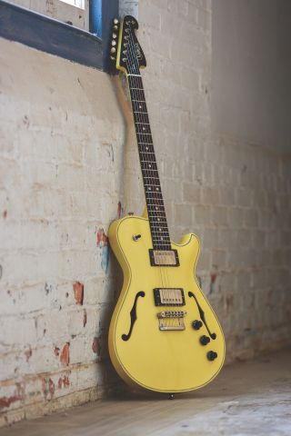 A yellow Maker Chena electric guitar leaning against a white brick wall