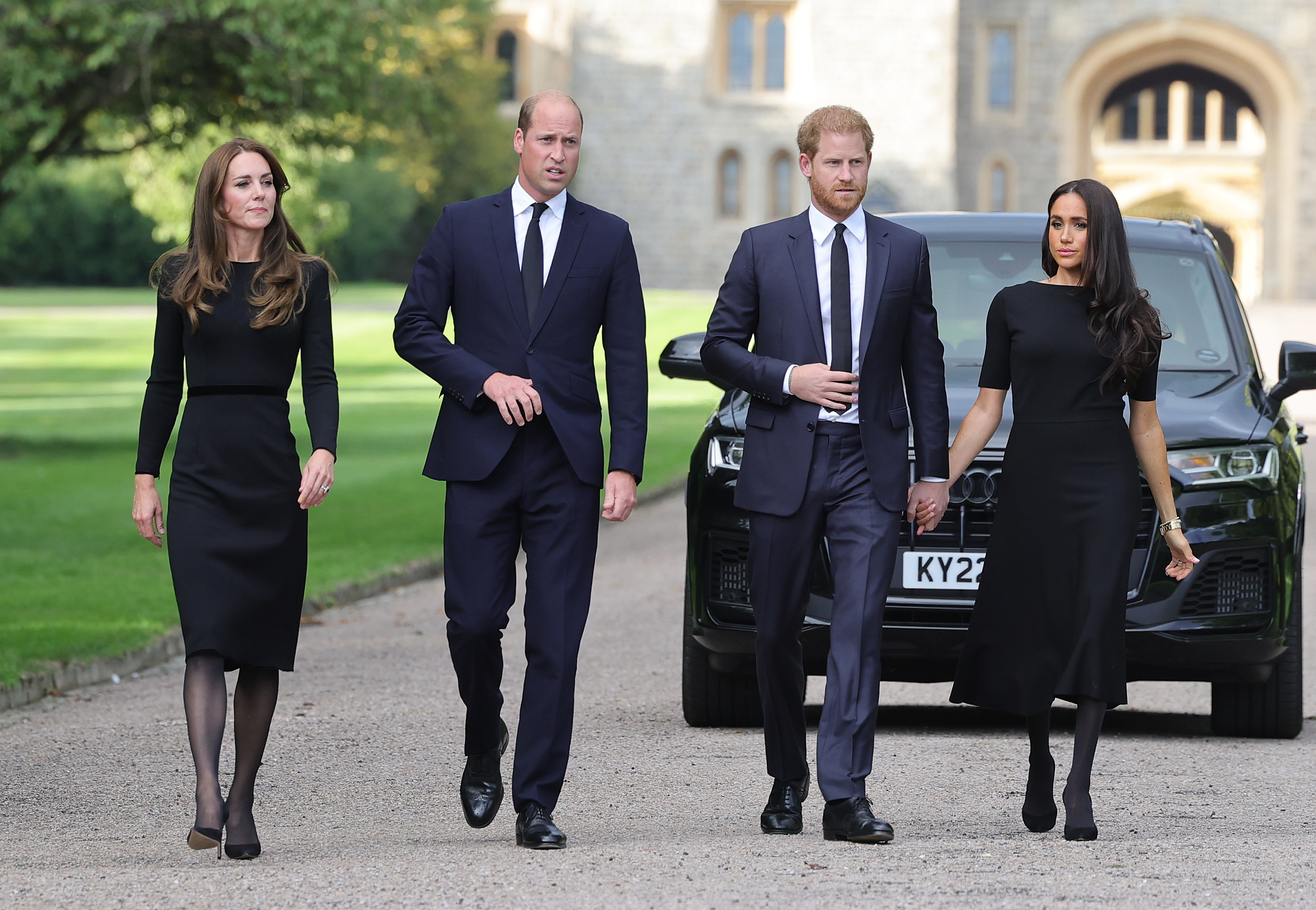 Princess Kate, Prince William, Prince Harry and Meghan Markle walking in front of a car