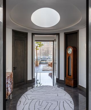 entry lobby with round skylight, oval patterned rug, wooden console and grandfather clock